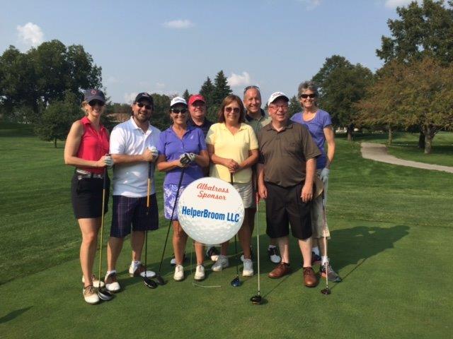 Group of 4 women and 4 men wearing shorts and holding golf clubs. In front of them is a sign in the image of a golf ball that reads "Albatross Sponsor: HeplerBroom LLC"