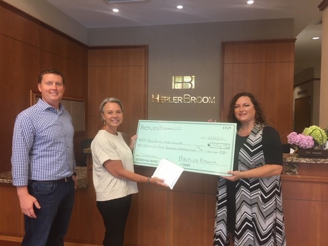 Lobby of HeplerBroom’s Edwardsville office with HeplerBroom partner Matt Champlin and paralegal Sandy Hammett presenting Equipping the Called co-founder Julie Tracy with a check