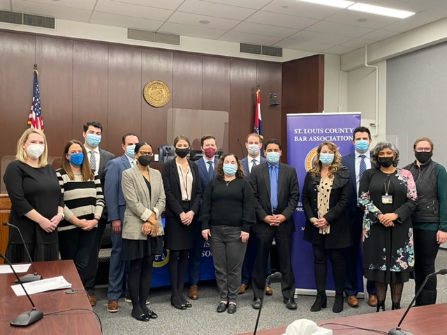 group of masked people in a courtroom with banner of St. Louis County Bar Association in background