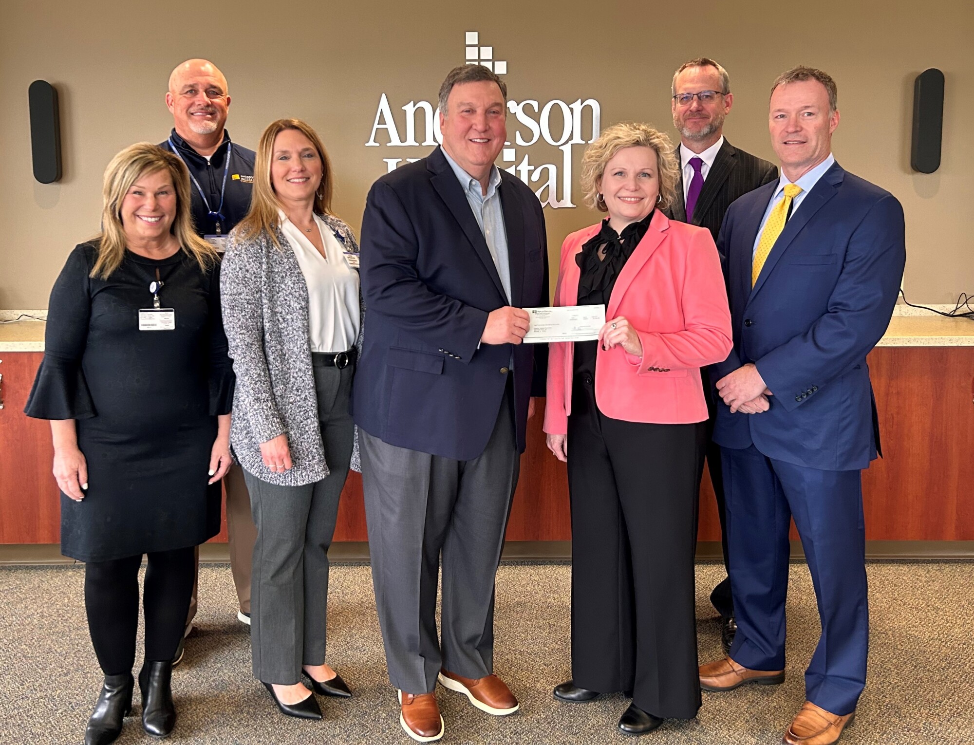 group of men and women with woman in center handing check to man in center