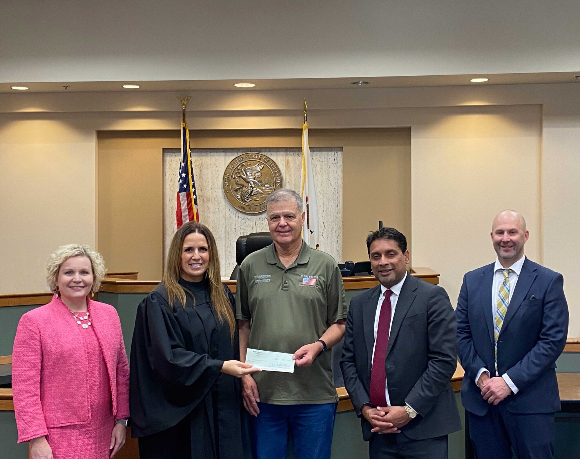 2 women and 3 men in a courtroom with 1 woman handing a check to one of the men