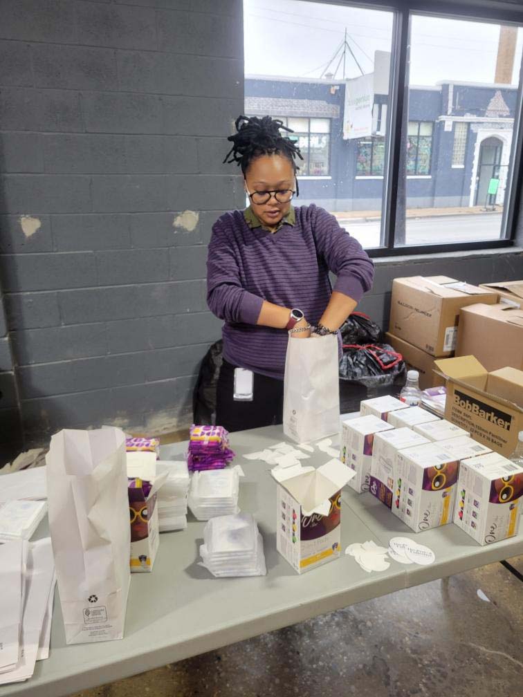 woman standing behind table putting products in to white bags