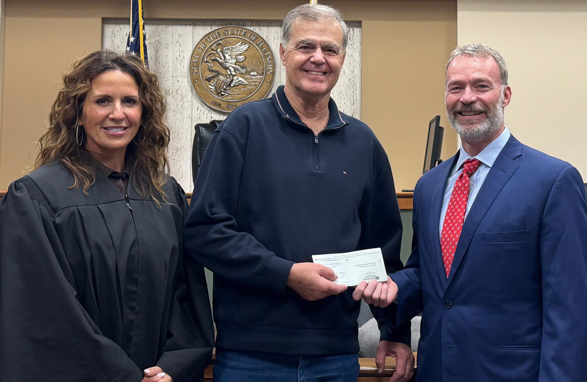 woman on left in judge's robes, men in center receiving check from man on right