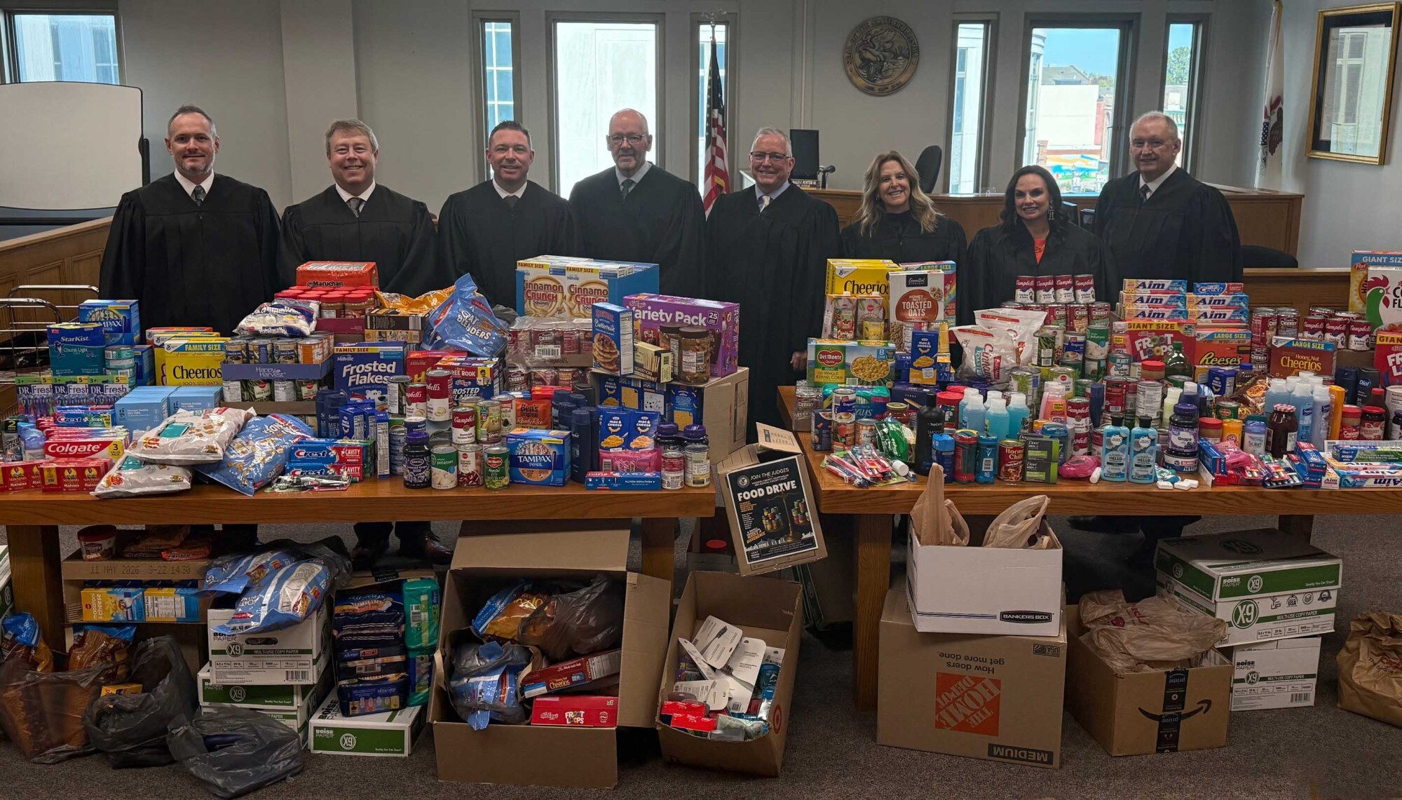 group of men and women in judges' robes standing behind multiple tables of food products