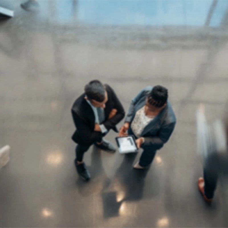 aerial view of 2 men in suits looking at a computer tablet betwen them